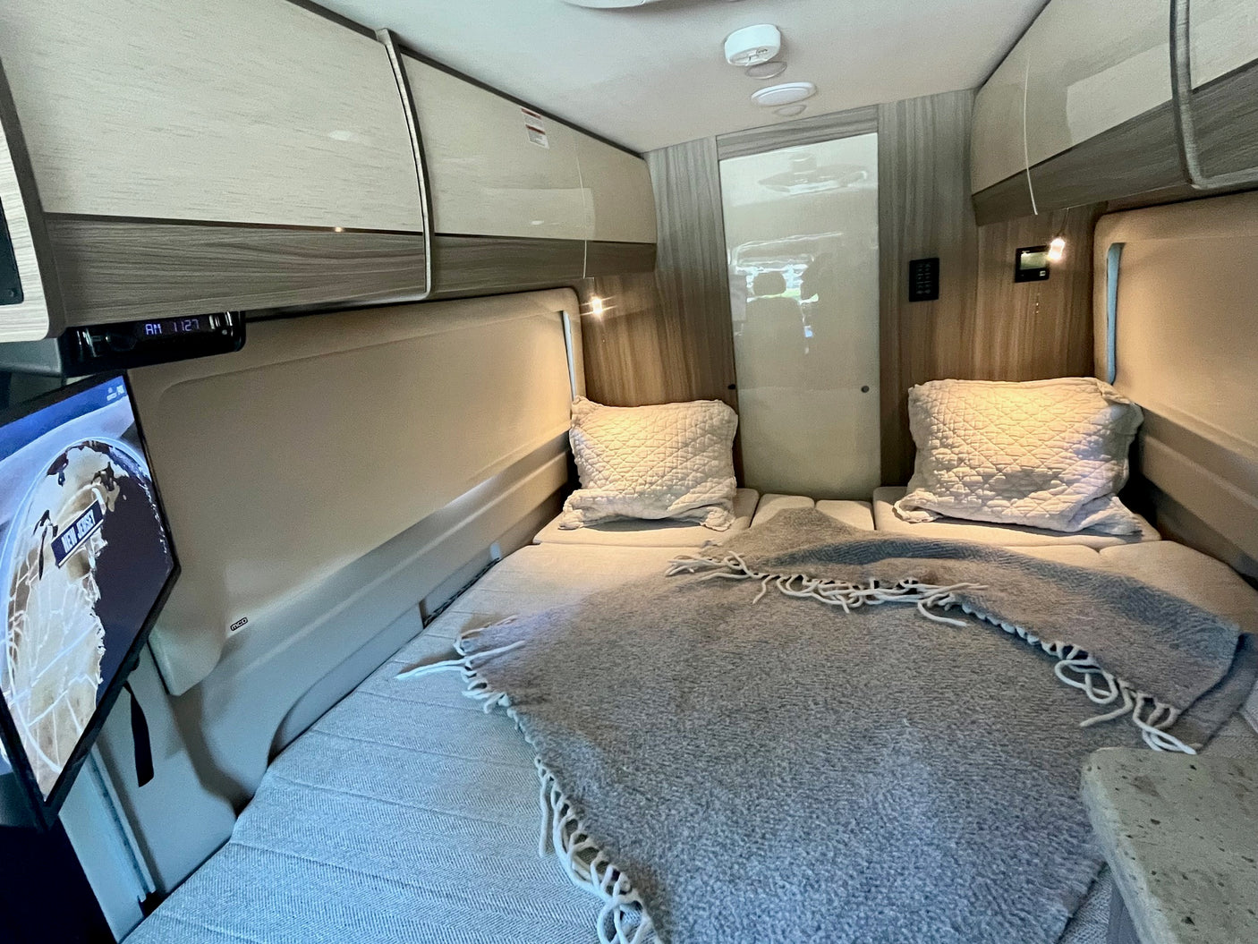 Inside this RV rental, find a modern bedroom with comfortable twin beds, overhead storage, and a TV for restful journeys.