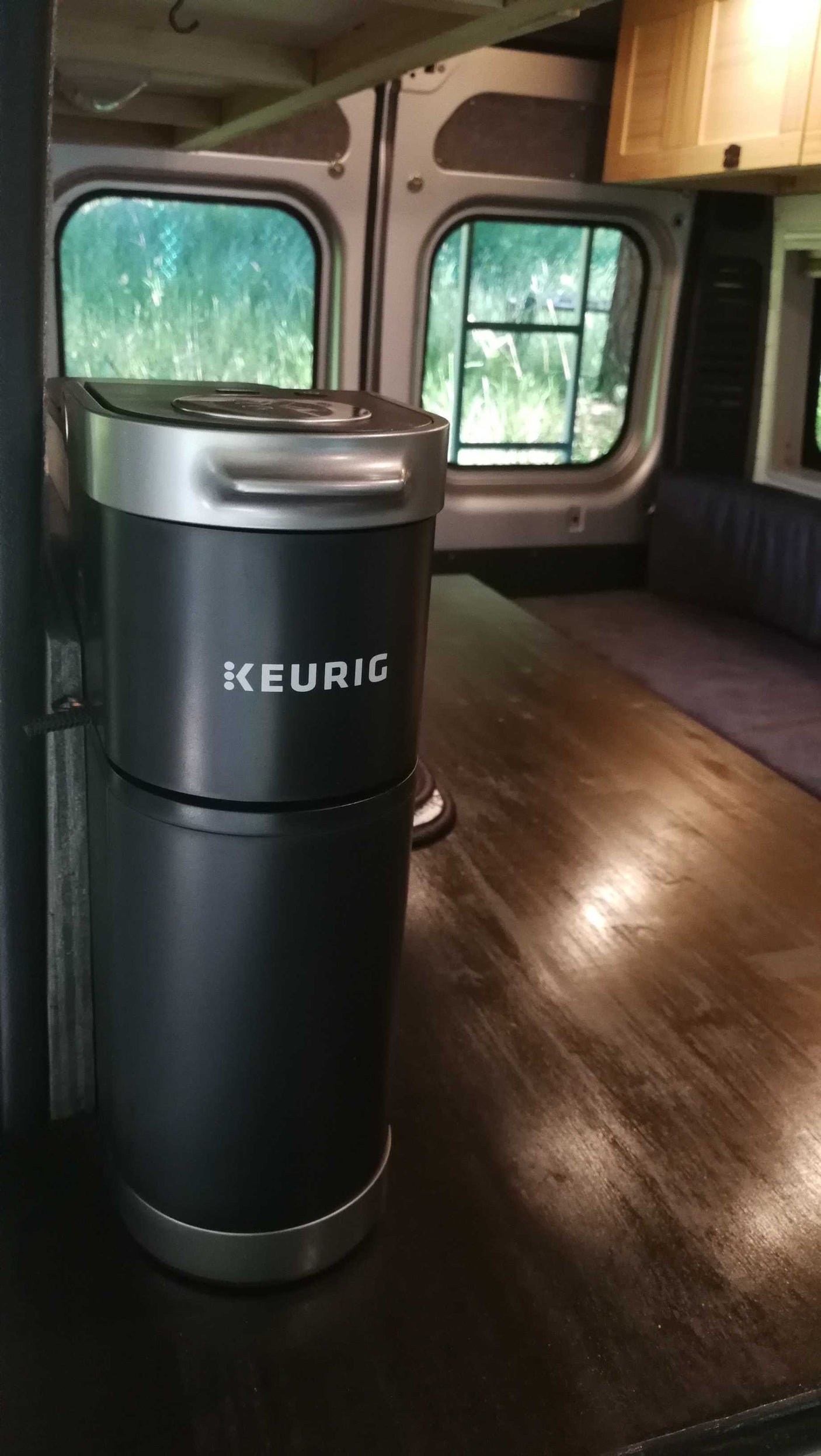 A black Keurig coffee maker sits on a wooden table inside an RV rental, offering coffee during camper van travels.