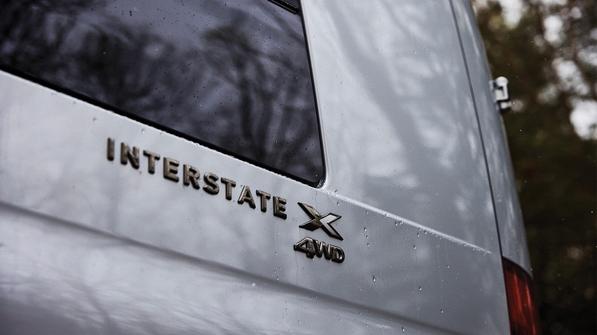 Rear view of a white Airstream Interstate X 4WD RV, ideal for an rv rental. Water droplets on the vehicle's surface imply rain.