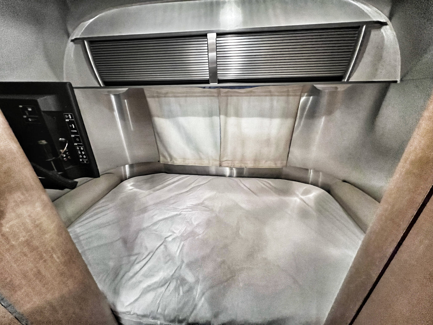 Cozy Airstream rv rental bedroom: a bed with white sheets, metallic walls, window blinds, and a control panel.