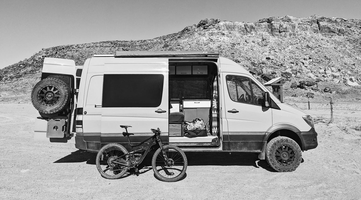 RV rental adventure: a rugged camper van and mountain bike parked in a rocky, arid landscape.