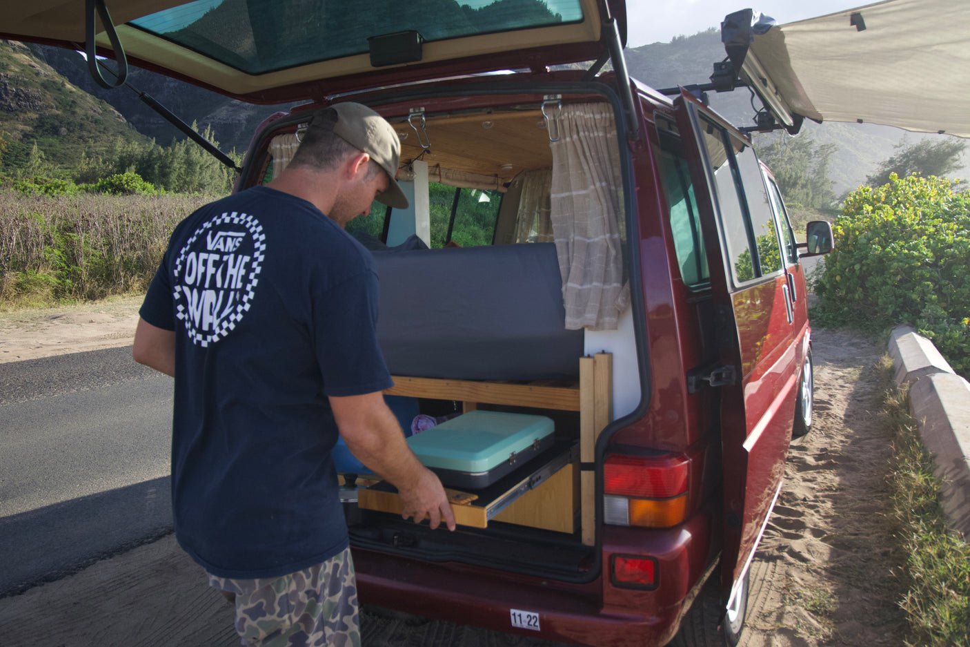 Man accessing portable kitchen from red RV rental. Perfect for van life adventures with stunning mountain views.