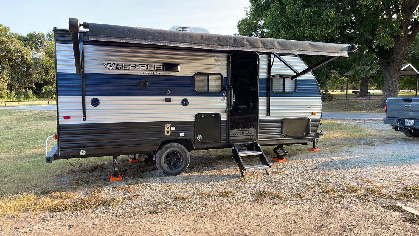 and extended awning.|A blue and white Wolf Pup travel trailer RV rental is parked at a gravel campsite. Awning extended