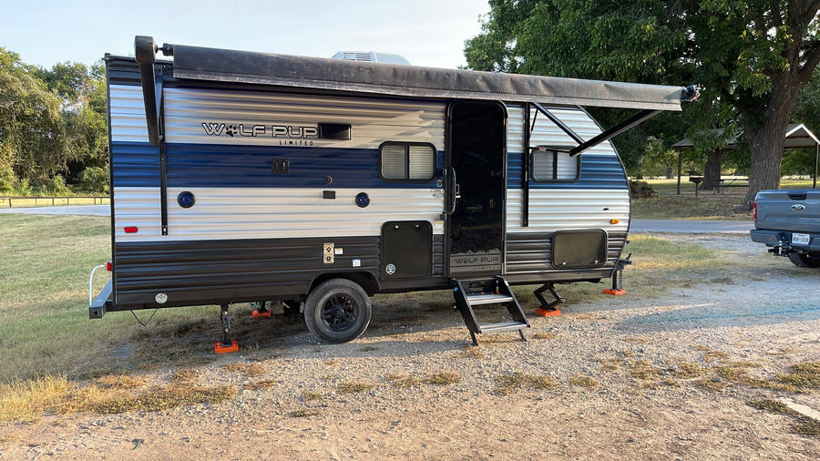 and extended awning.|A blue and white Wolf Pup travel trailer RV rental is parked at a gravel campsite. Awning extended