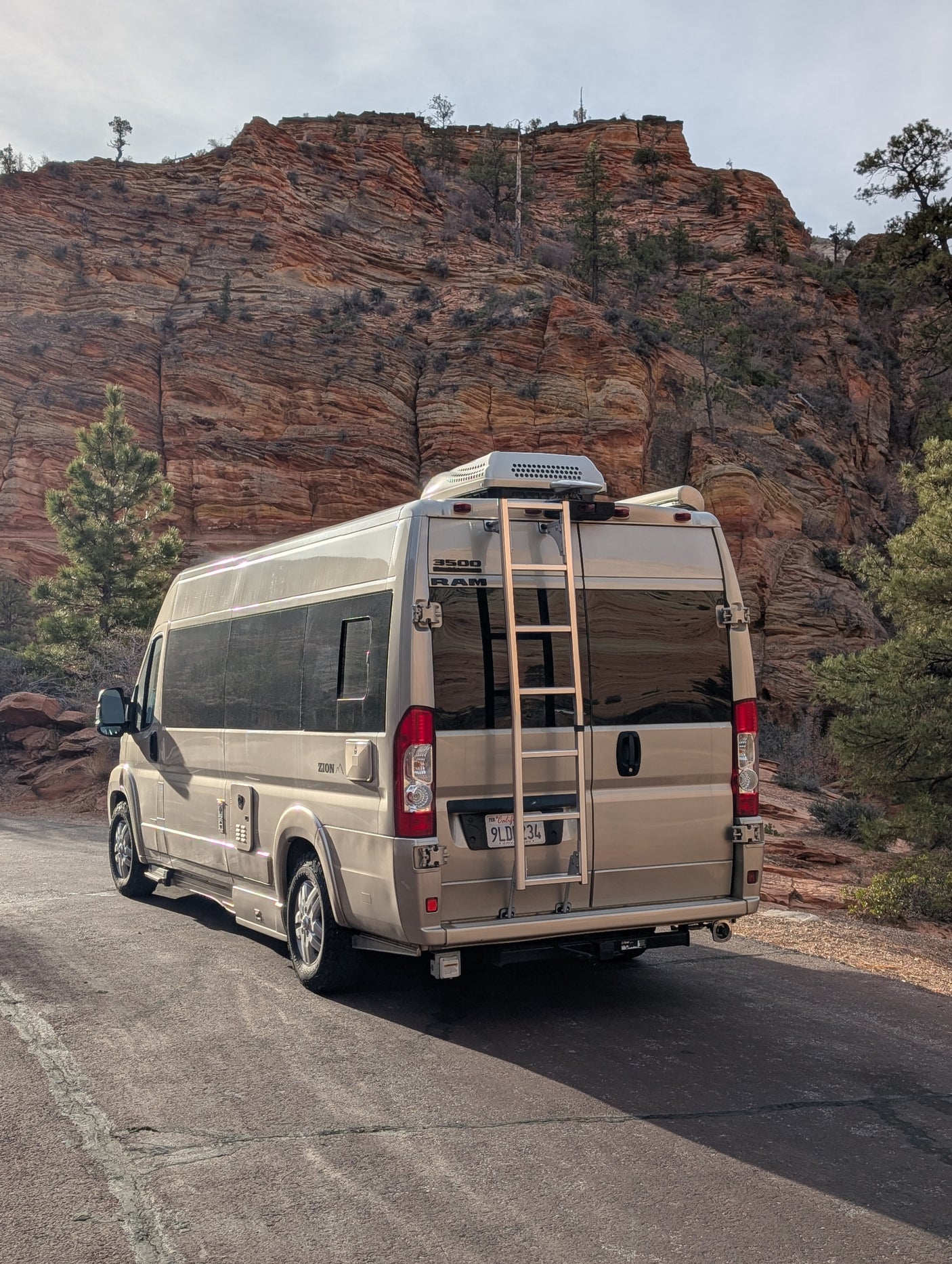 Tan RV rental van parked on a scenic road with majestic red rock mountains in the background.