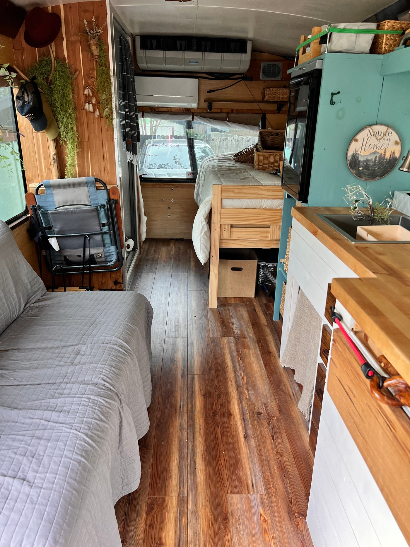 Inside a custom RV rental: wooden interior with a bed, daybed, kitchen, and two AC units visible. — photo 12
