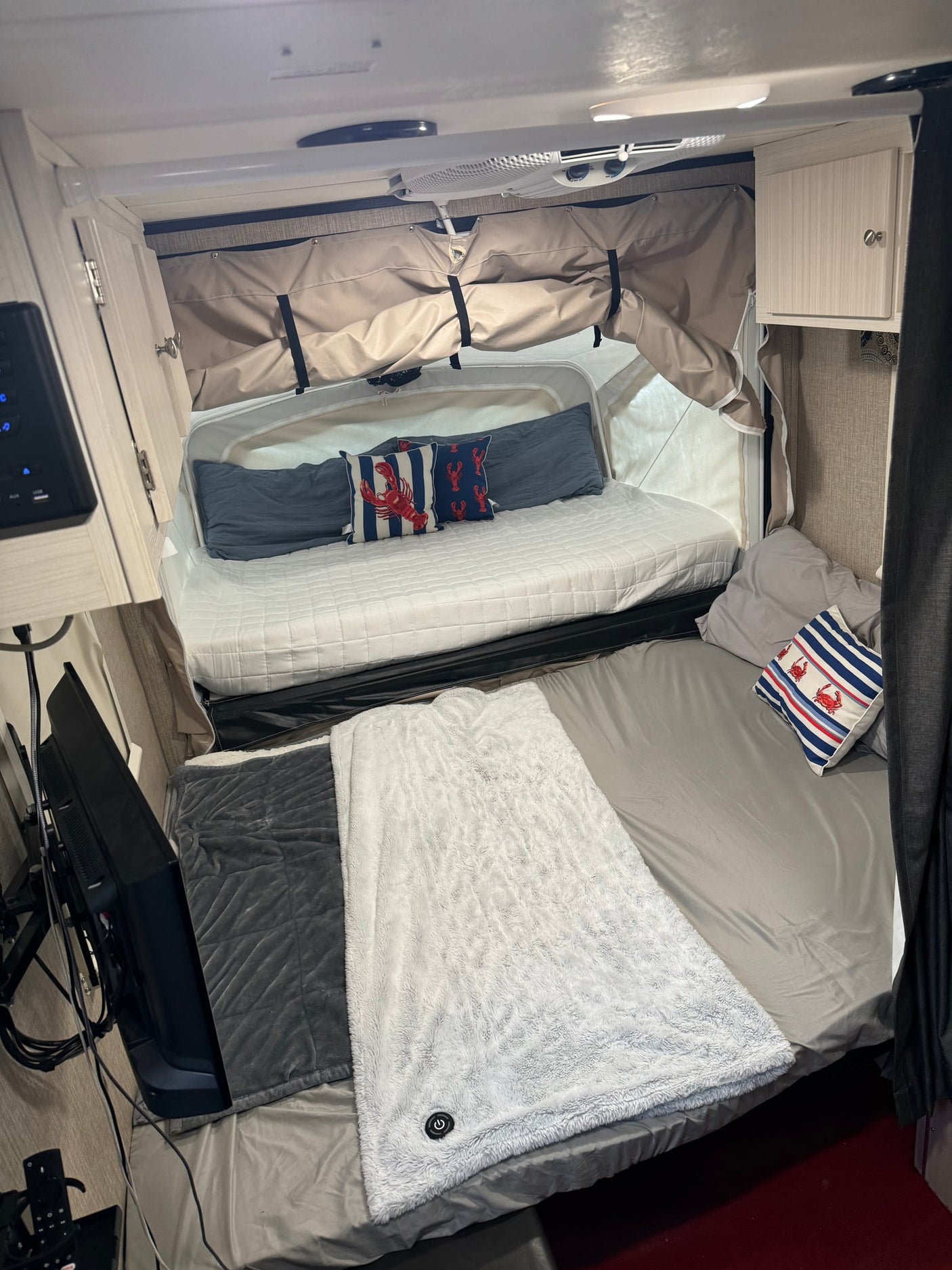 Inviting rv rental sleeping area with two beds: one pop-out, one standard. Cozy blankets, nautical pillows, TV, and cabinets visible.