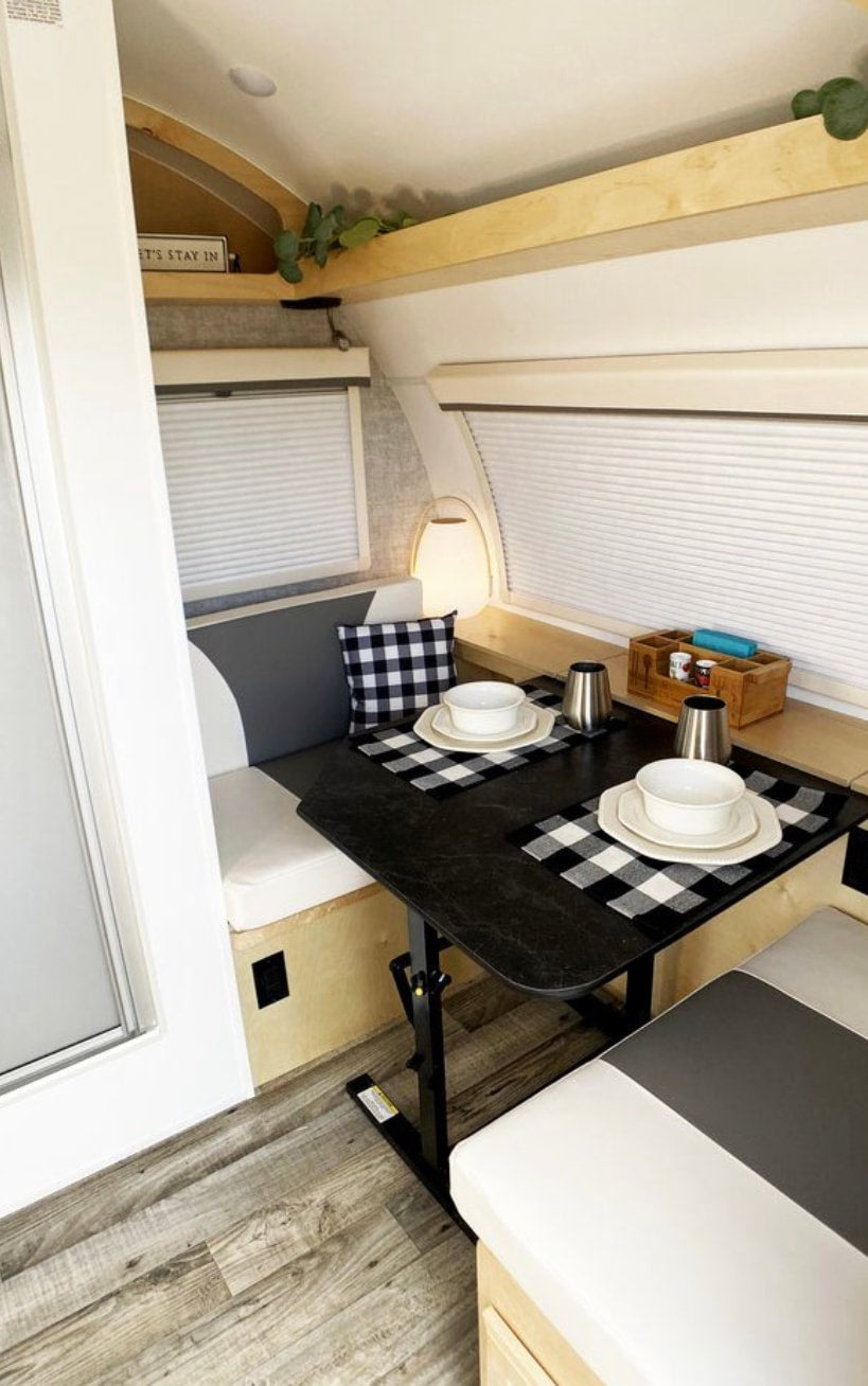 Cozy RV rental dinette with a black table, two white & gray benches, and buffalo check placemats. Ideal for compact travel.