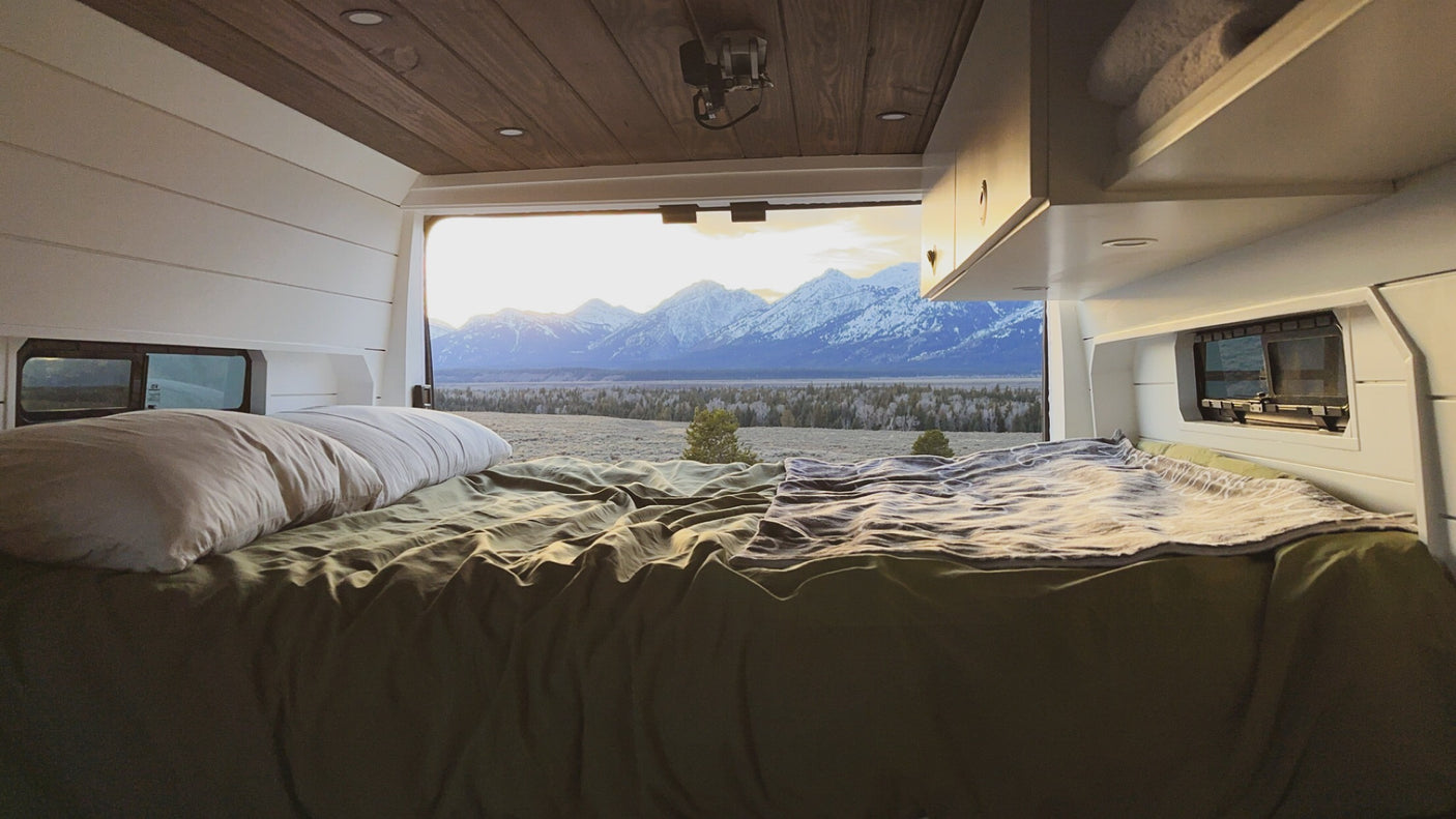Relax in an RV rental bed with stunning views of snow-capped mountains at sunrise/sunset. Perfect for memorable adventures.|Bright RV rental interior features dark wood ceiling & counters