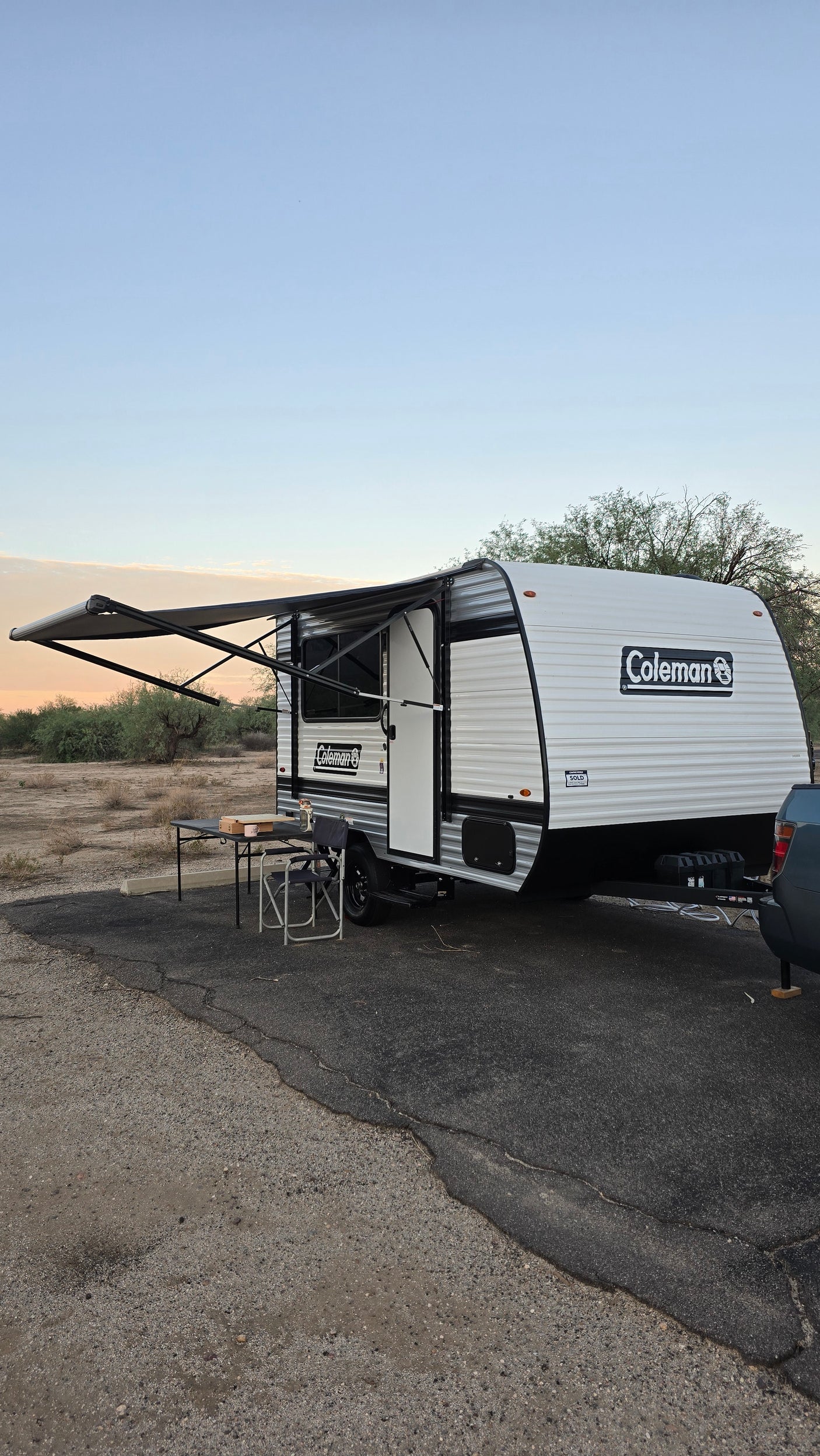 RV rental: A Coleman travel trailer with awning extended, table & chair outside, parked in a desert setting.