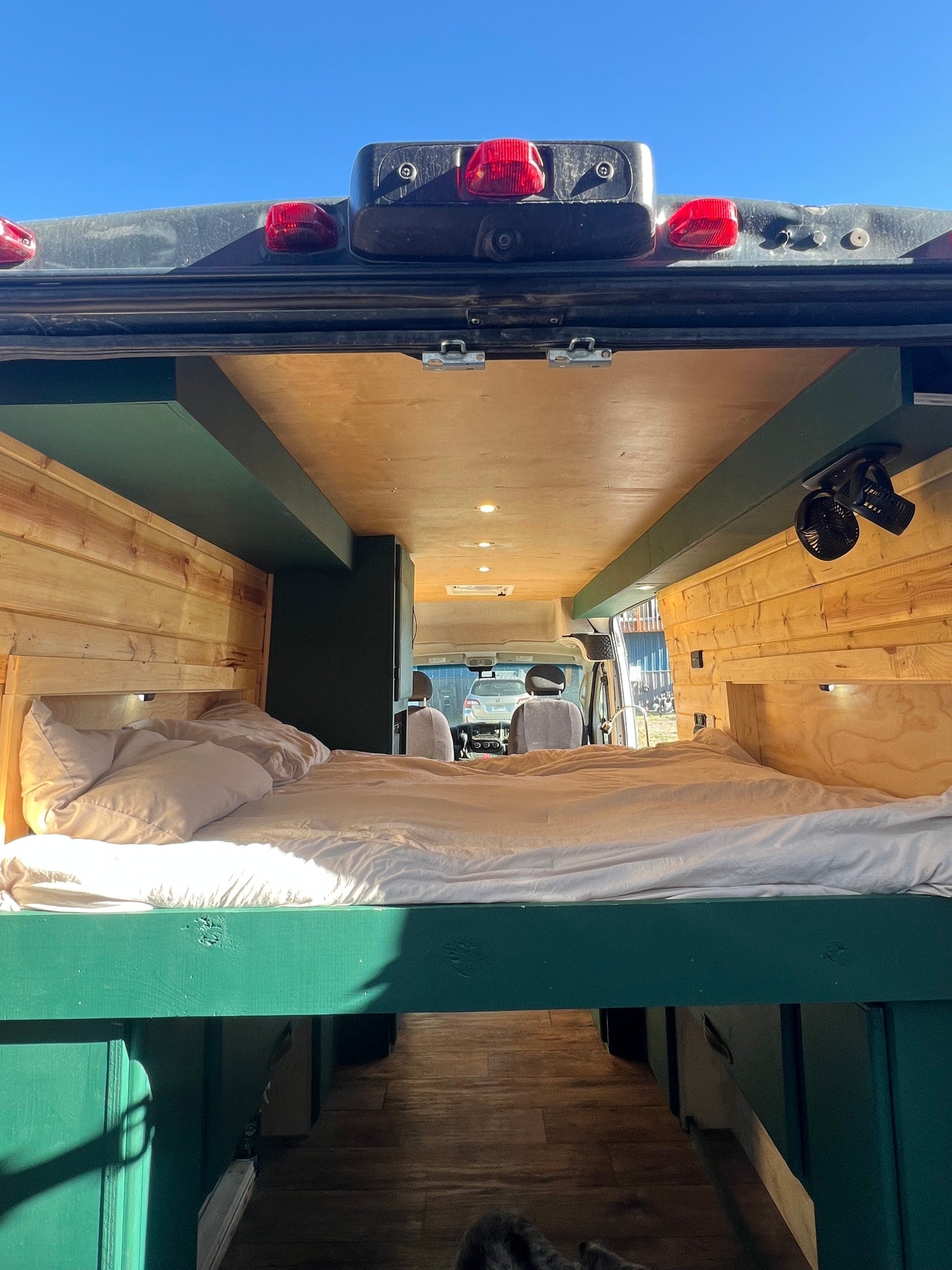 Cozy RV rental interior with a comfortable bed, wood paneling, and a view to the front cabin. Perfect for mobile adventures.
