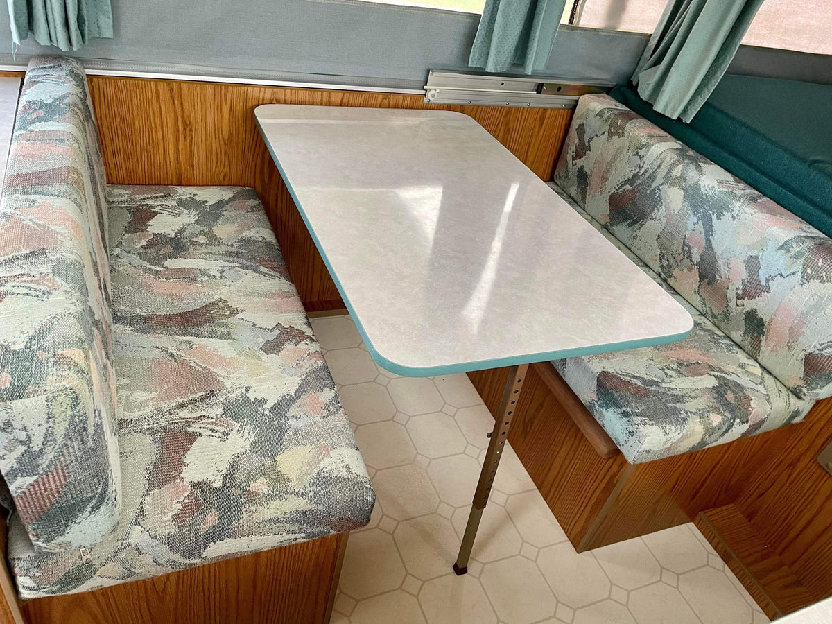 RV rental interior: A camper's dinette area features a light table, patterned benches, and wood paneling. — photo 3