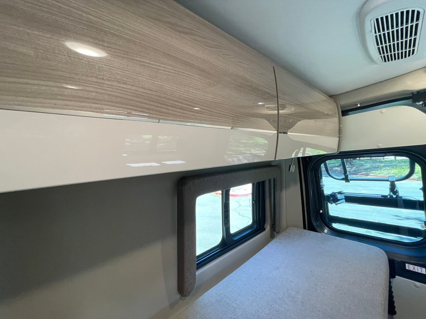 Modern RV rental interior featuring overhead cabinets, a cozy bed, and large windows for a comfortable camper van experience.