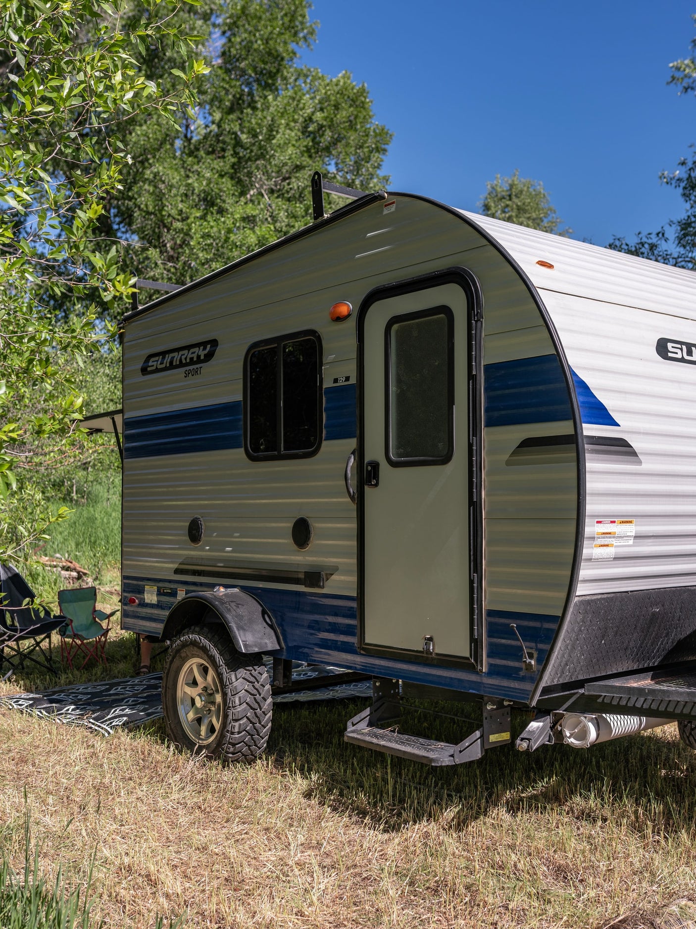 SunRay Sport RV rental trailer parked in a sunny, tree-lined campsite. Ready for your next outdoor adventure.