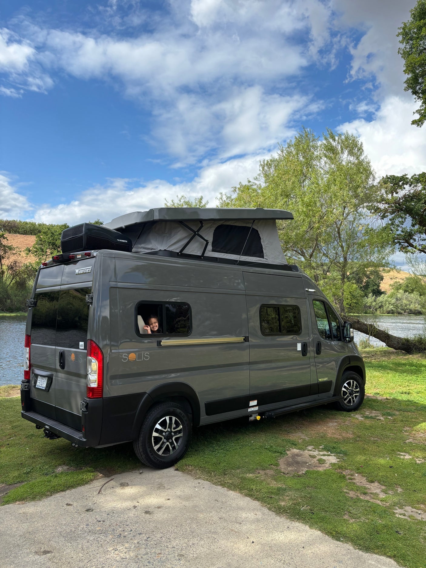 Winnebago Solis RV rental parked riverside, with a happy child waving from the window.