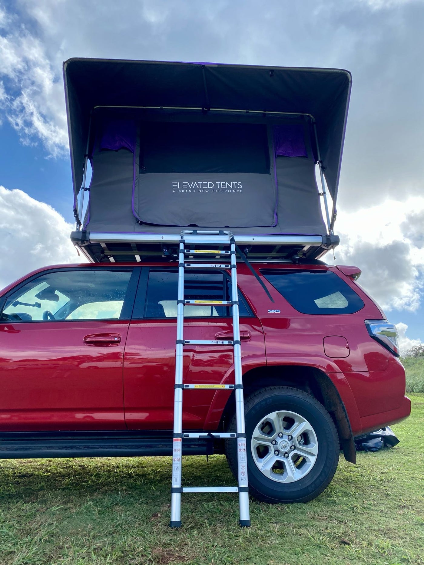 Red Toyota 4Runner SUV with an 'Elevated Tents' rooftop tent deployed and ladder extended, ideal for an RV rental outdoor adventure. — photo 4
