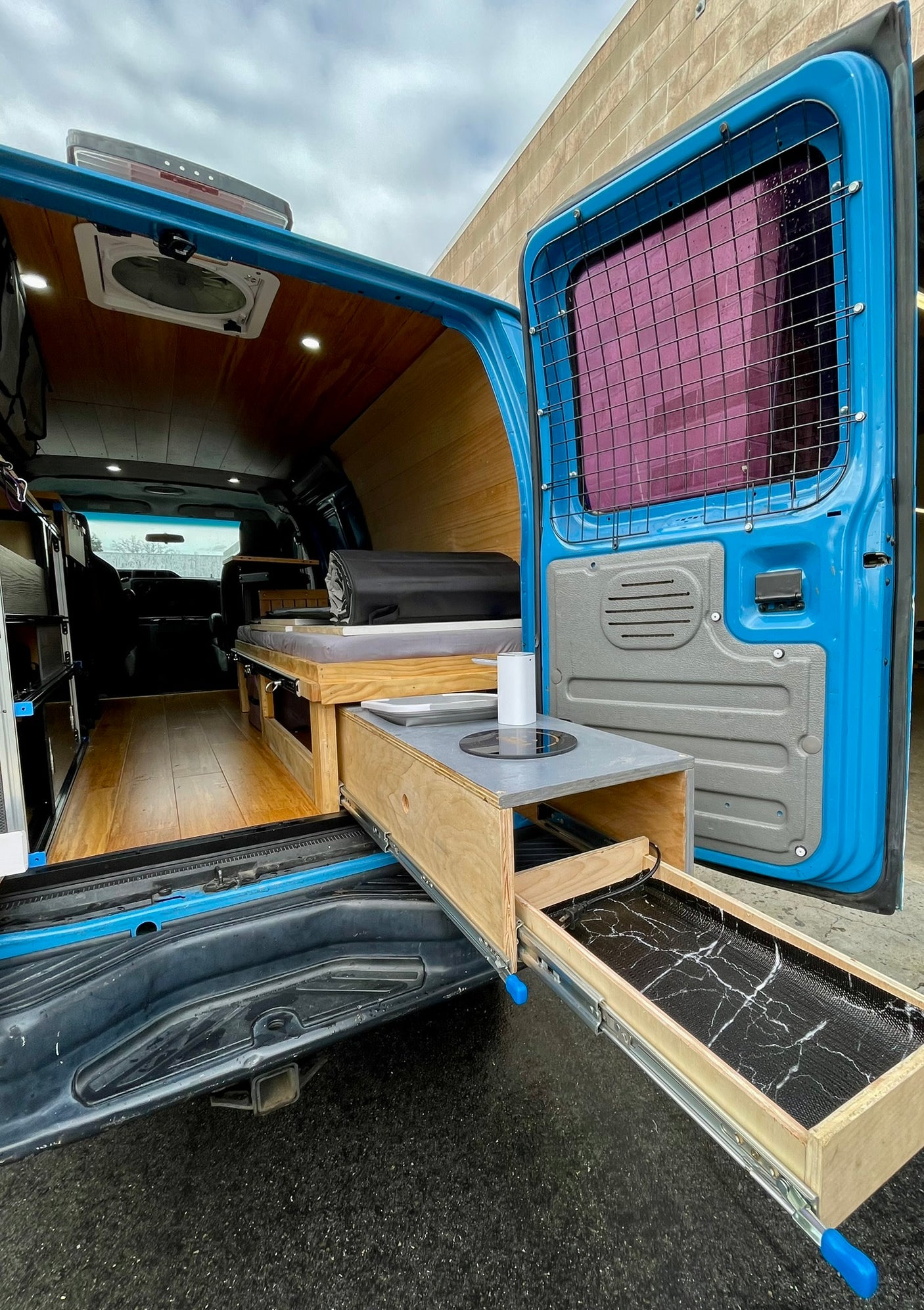 RV rental-ready blue camper van interior featuring a pull-out kitchen, bed, and stylish wood-paneled walls.