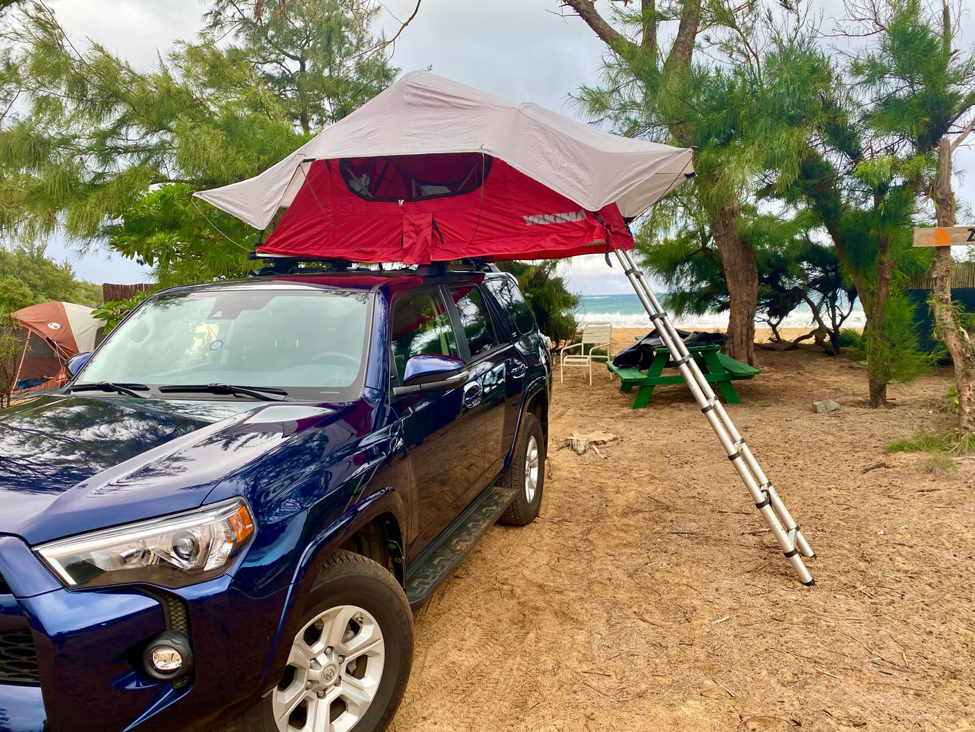 Beachside RV rental: blue SUV with rooftop tent deployed for sandy camping by the ocean.