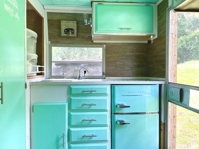 complete with a Magic Chef fridge & scenic window views.|Inside this cute **RV rental**: a mint green & wood retro camper kitchen with fridge & patterned ceiling.|Cozy RV rental interior featuring a built-in dinette with grey cushions