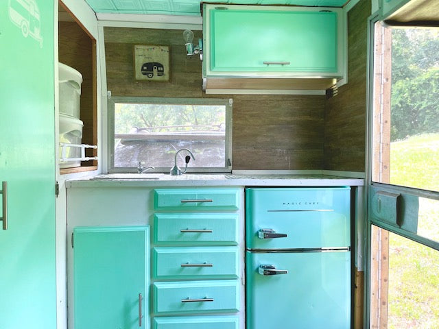 complete with a Magic Chef fridge & scenic window views.|Inside this cute **RV rental**: a mint green & wood retro camper kitchen with fridge & patterned ceiling.|Cozy RV rental interior featuring a built-in dinette with grey cushions