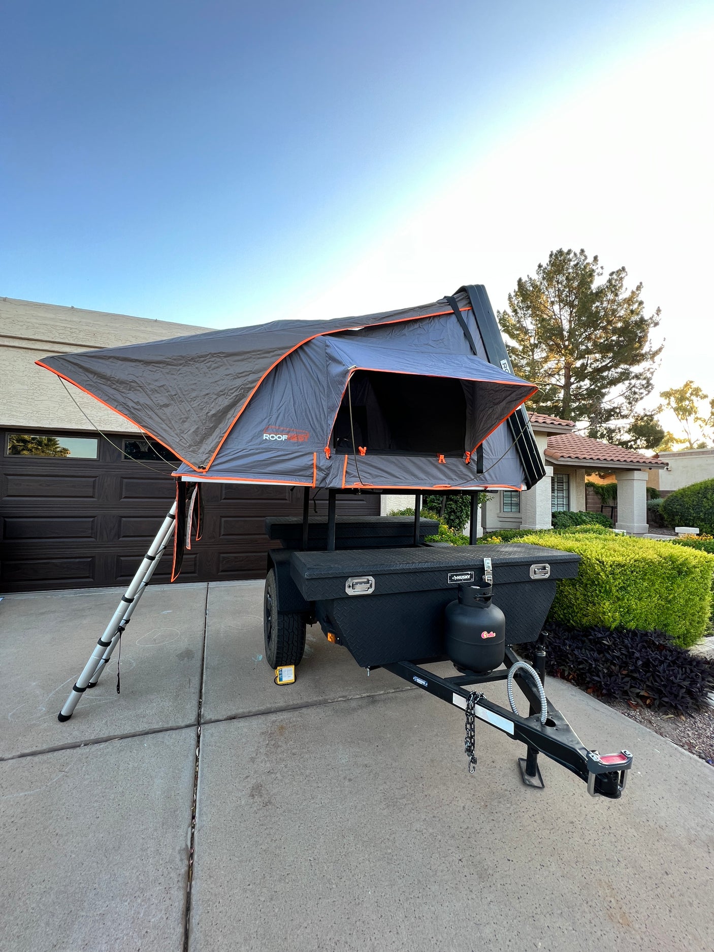 Grey rooftop tent set up on a black camping trailer with gear. A compact RV rental alternative for overland adventures.