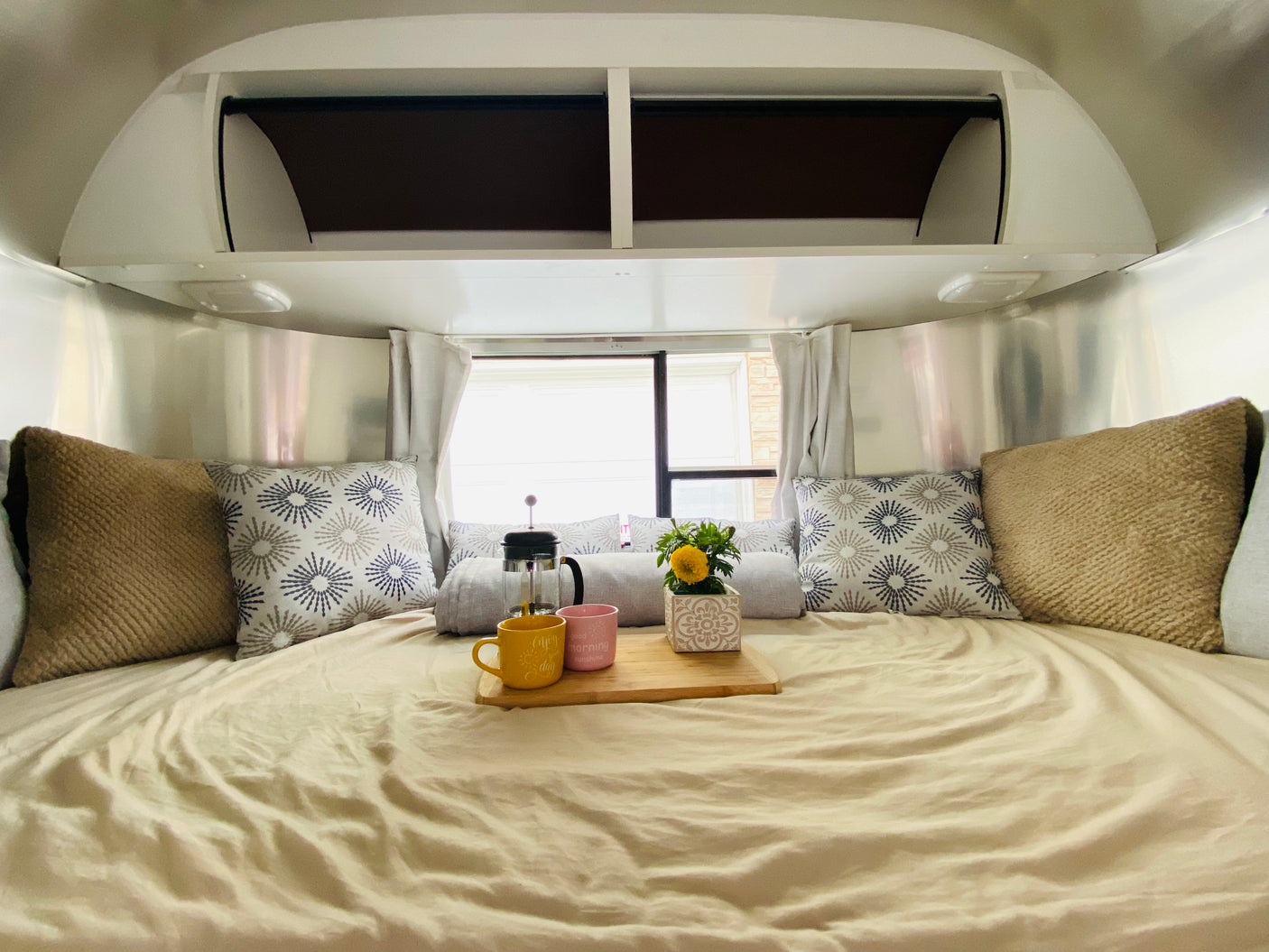 Experience a cozy RV rental: bedroom with polished walls, plush pillows, and a French press breakfast in bed.