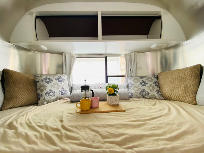 Experience a cozy RV rental: bedroom with polished walls, plush pillows, and a French press breakfast in bed.