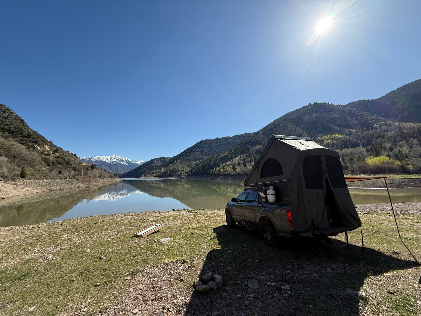 A truck with a rooftop tent is set up for camping beside a calm mountain lake, an adventurous **RV rental** alternative.
