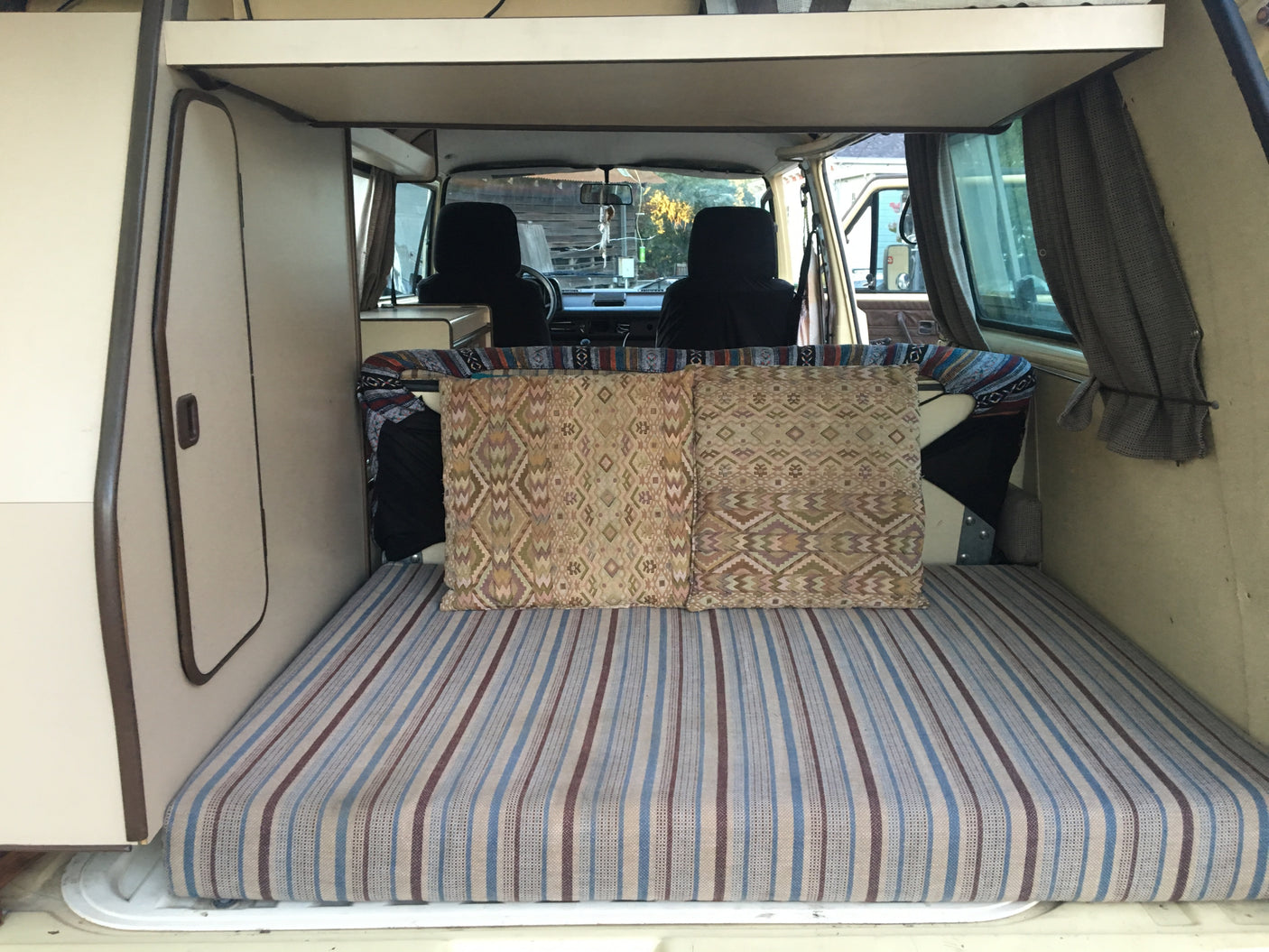 Inside an rv rental: View from the rear of a camper van, showing a striped bed, decorative pillows, and front seats.