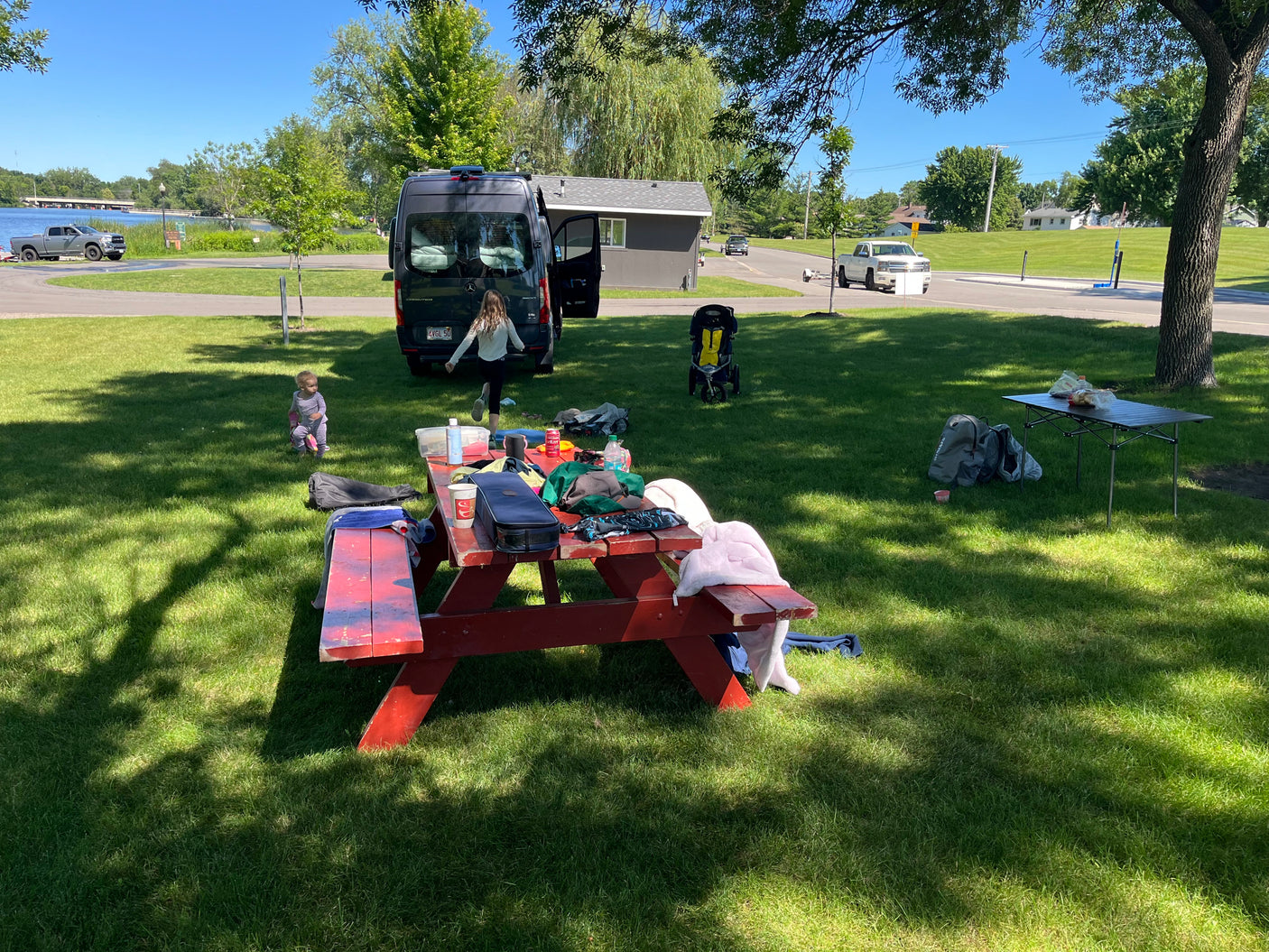 Family enjoying a sunny day outdoors with their RV rental (Mercedes Sprinter van) at a park, featuring a picnic table and kids playing.