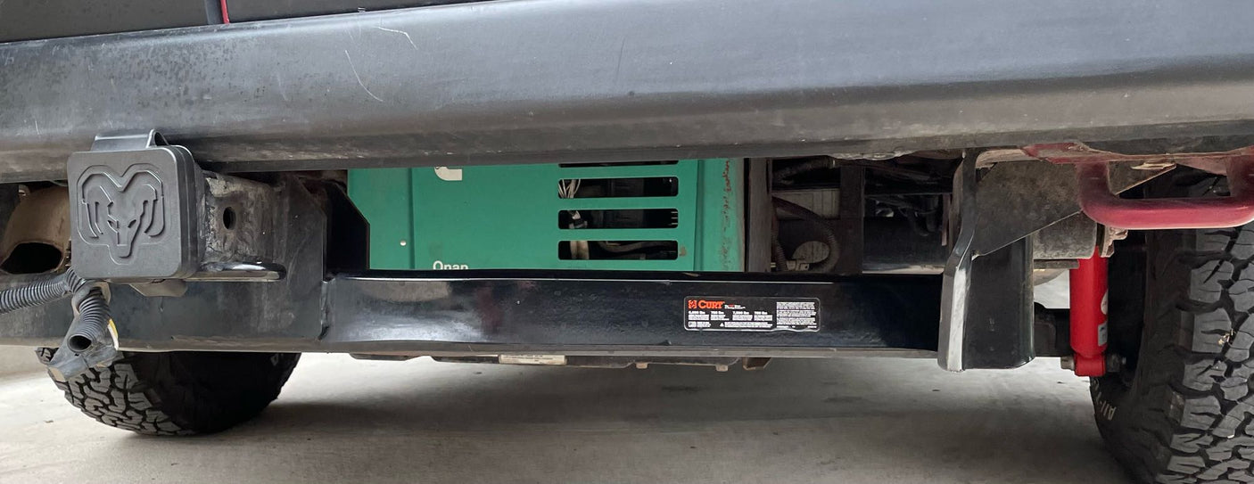 Underside view of an RV rental, showing an Onan generator, Curt hitch, and Ram logo cap. Ready for travel.