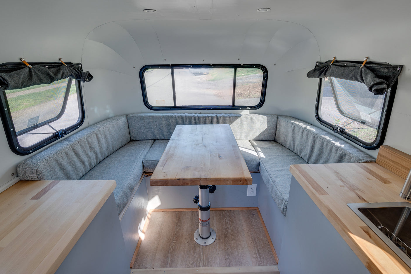 RV rental: Light-filled interior with U-shaped dinette, adjustable wood table, and compact kitchen area.