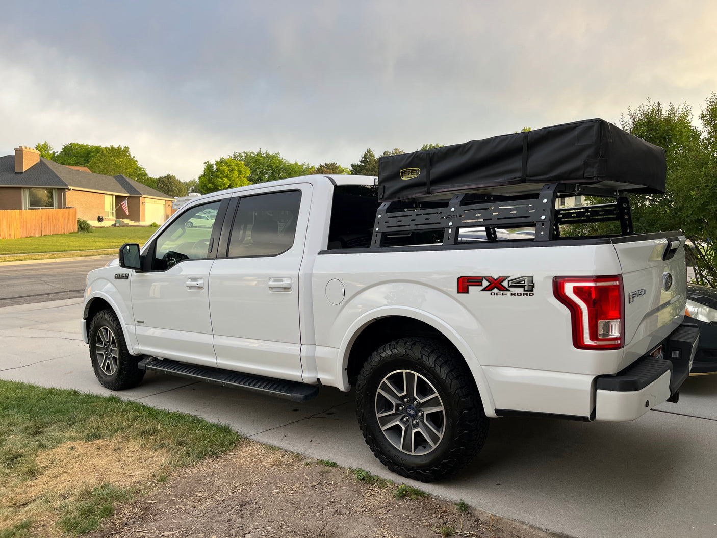 White Ford F-150 pickup with rooftop tent & bed rack, parked on a driveway. Perfect for overlanding; explore 'rv rental' for adventure vehicles.