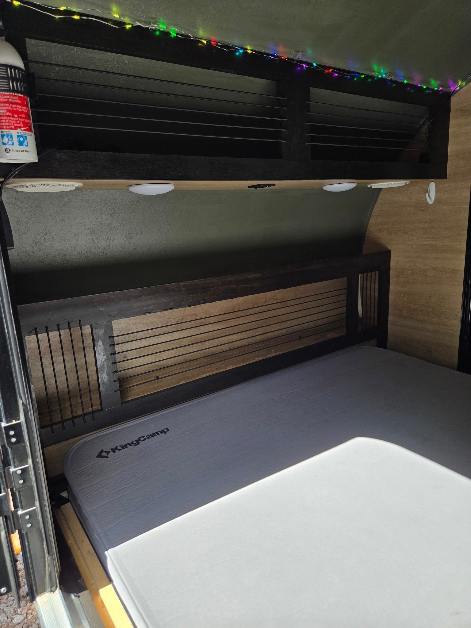 RV rental: KingCamp mattress, slatted headboard, overhead storage with colorful string lights & First Alert extinguisher.