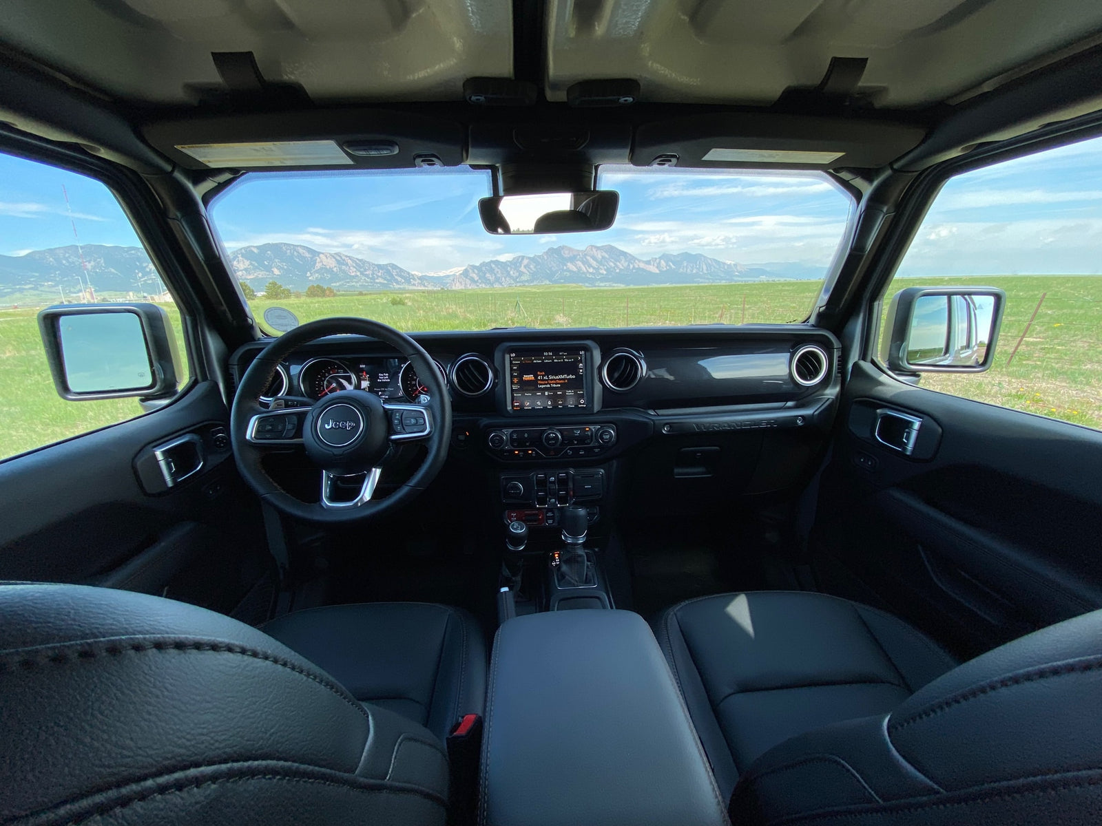 Inside a Jeep Wrangler, showing dashboard and steering wheel, with vast mountains and green fields. Perfect for adventure, like an RV rental trip.