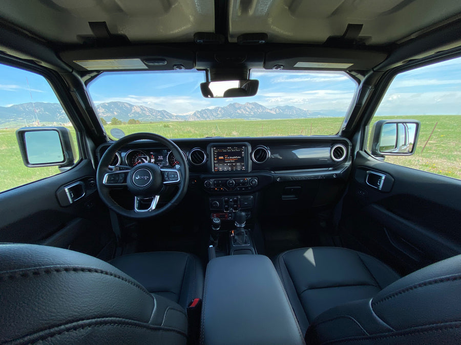 Inside a Jeep Wrangler, showing dashboard and steering wheel, with vast mountains and green fields. Perfect for adventure, like an RV rental trip.
