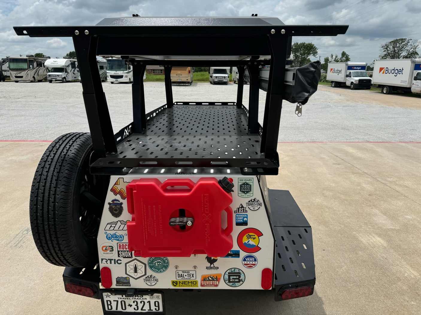 Overland trailer loaded with gear, parked near RVs and Budget RV rental trucks, ready for outdoor adventure.