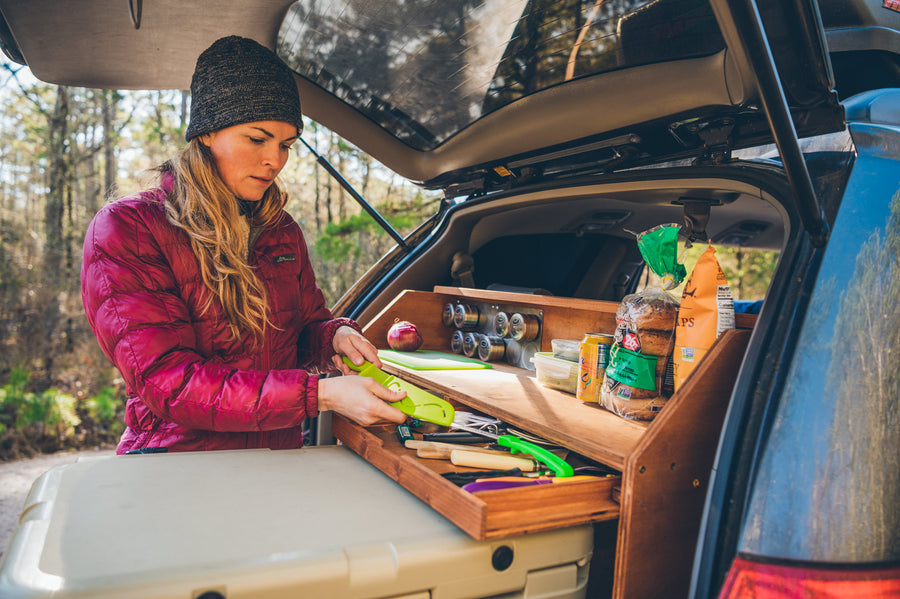 and coffee pot ready. Ideal for any RV rental adventure.|Woman prepares food using a custom portable kitchen in an SUV trunk