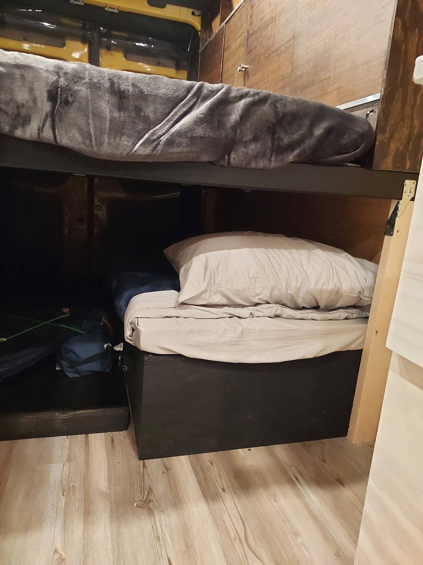 RV rental interior: Wooden walls, black storage, and neatly stored bedding with a blue bag in a compact space.