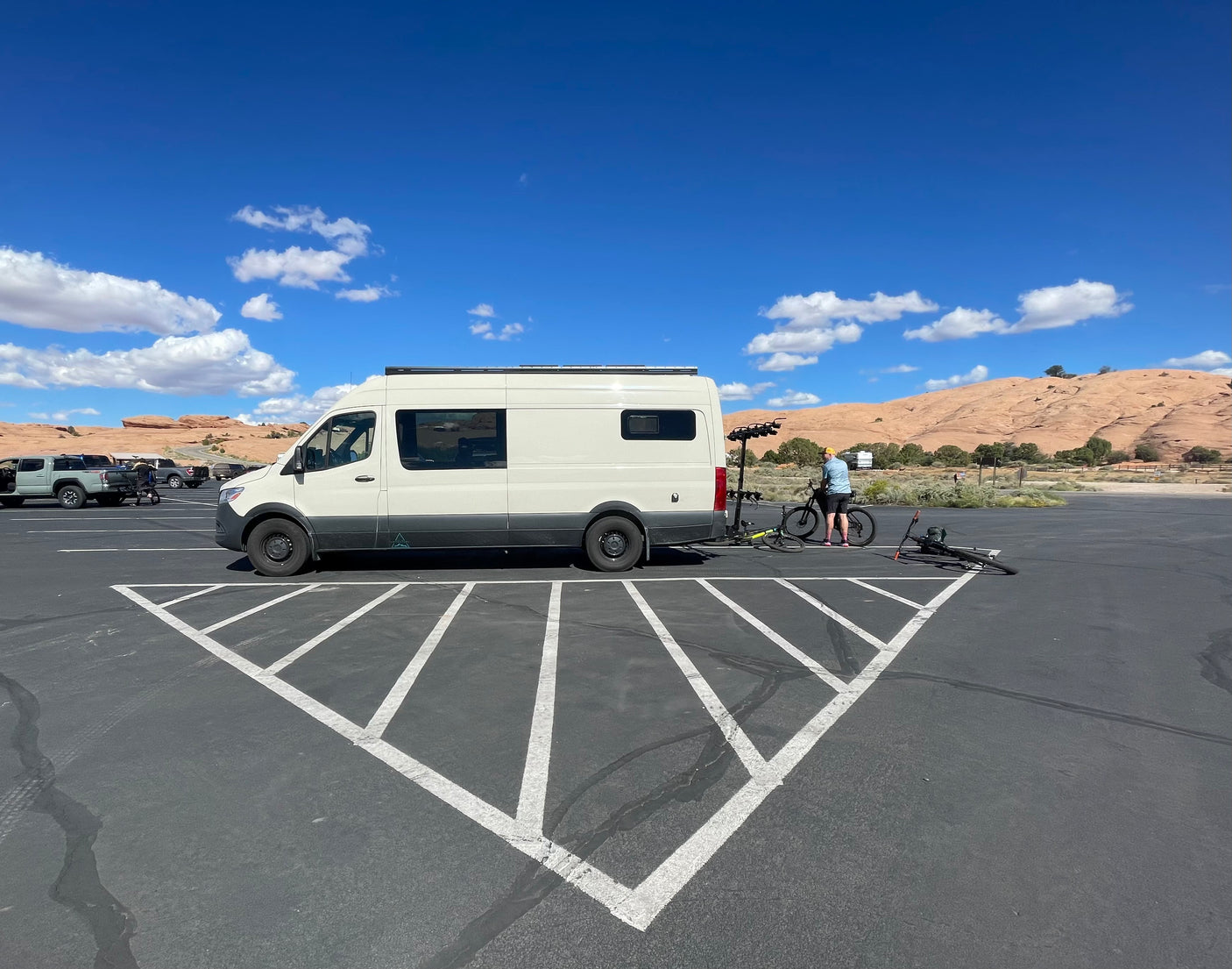 An RV rental camper van parked in a desert lot. A person prepares bikes for outdoor adventure against a scenic backdrop.