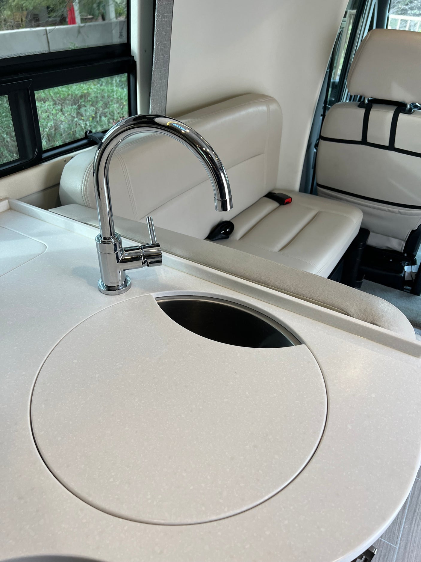 Explore this RV rental's bright interior! Modern kitchenette with white counter, chrome faucet, & integrated sink/cover, plus comfy seats.