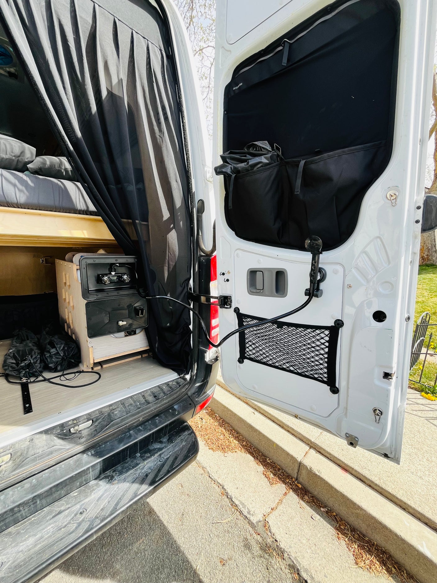Open back of an RV rental: custom bed, portable sink, and outdoor shower on the door. Ready for your van life adventure.