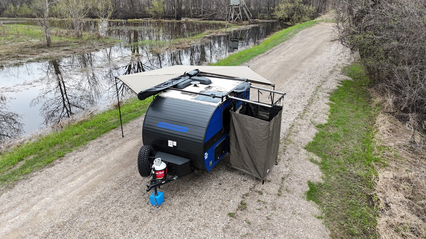 This RV rental teardrop camper, with an awning & privacy tent, is ready for adventure by a scenic marsh.