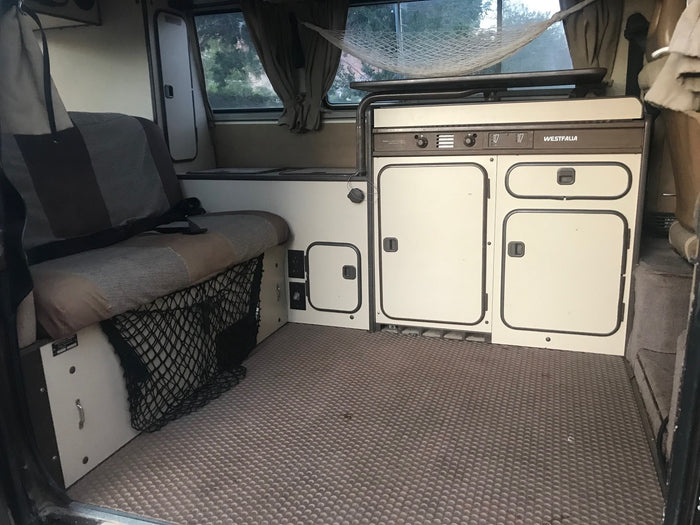 dark VW Vanagon pop-top camper van with off-road tires and an awning