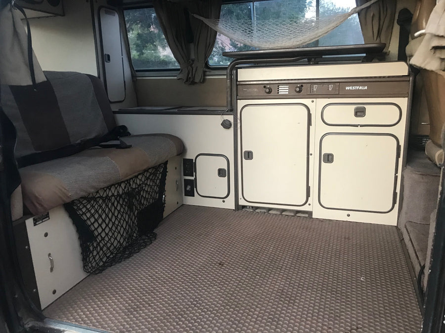 dark VW Vanagon pop-top camper van with off-road tires and an awning