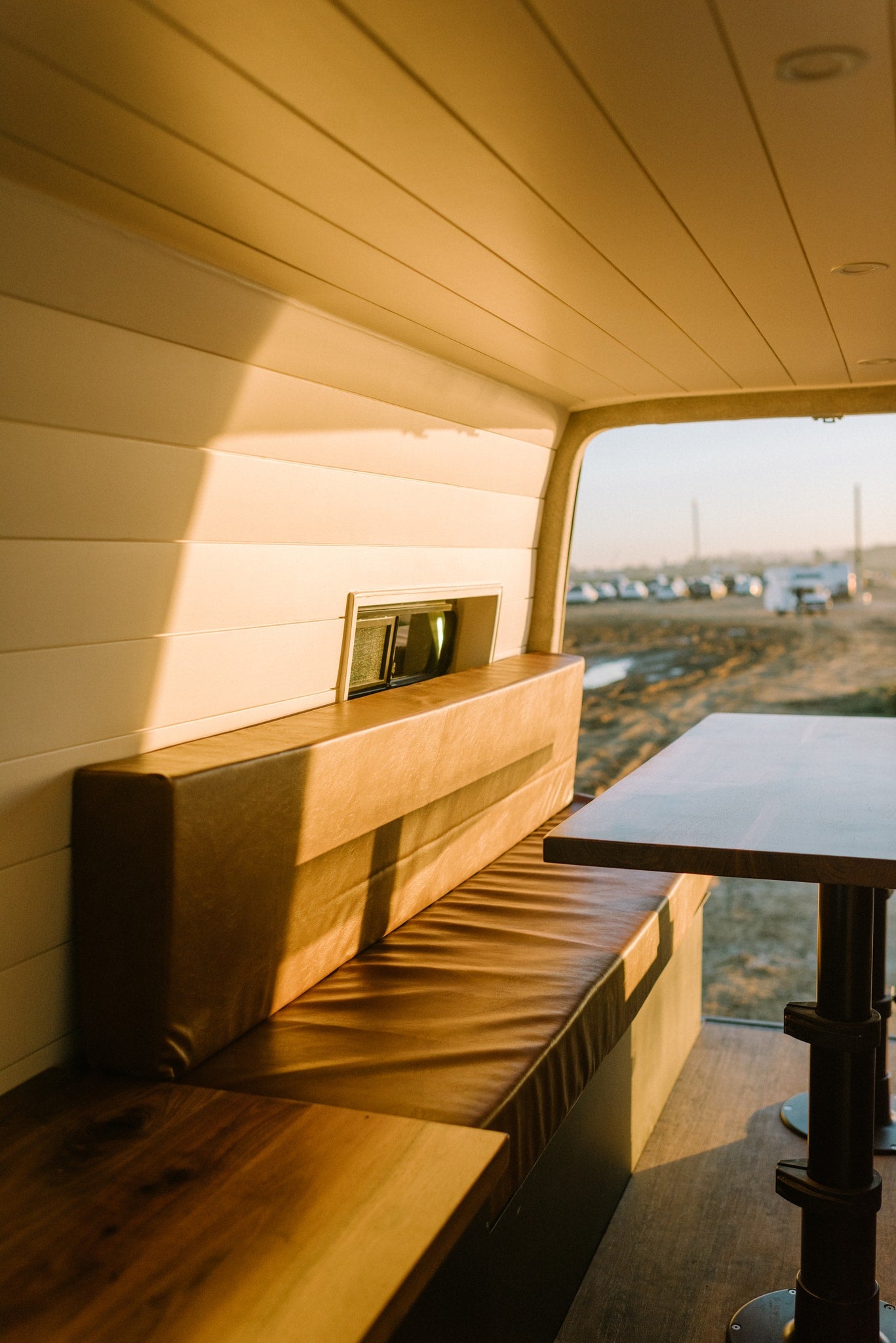 A comfortable brown bench and wooden table within a modern rv rental van interior. — photo 14