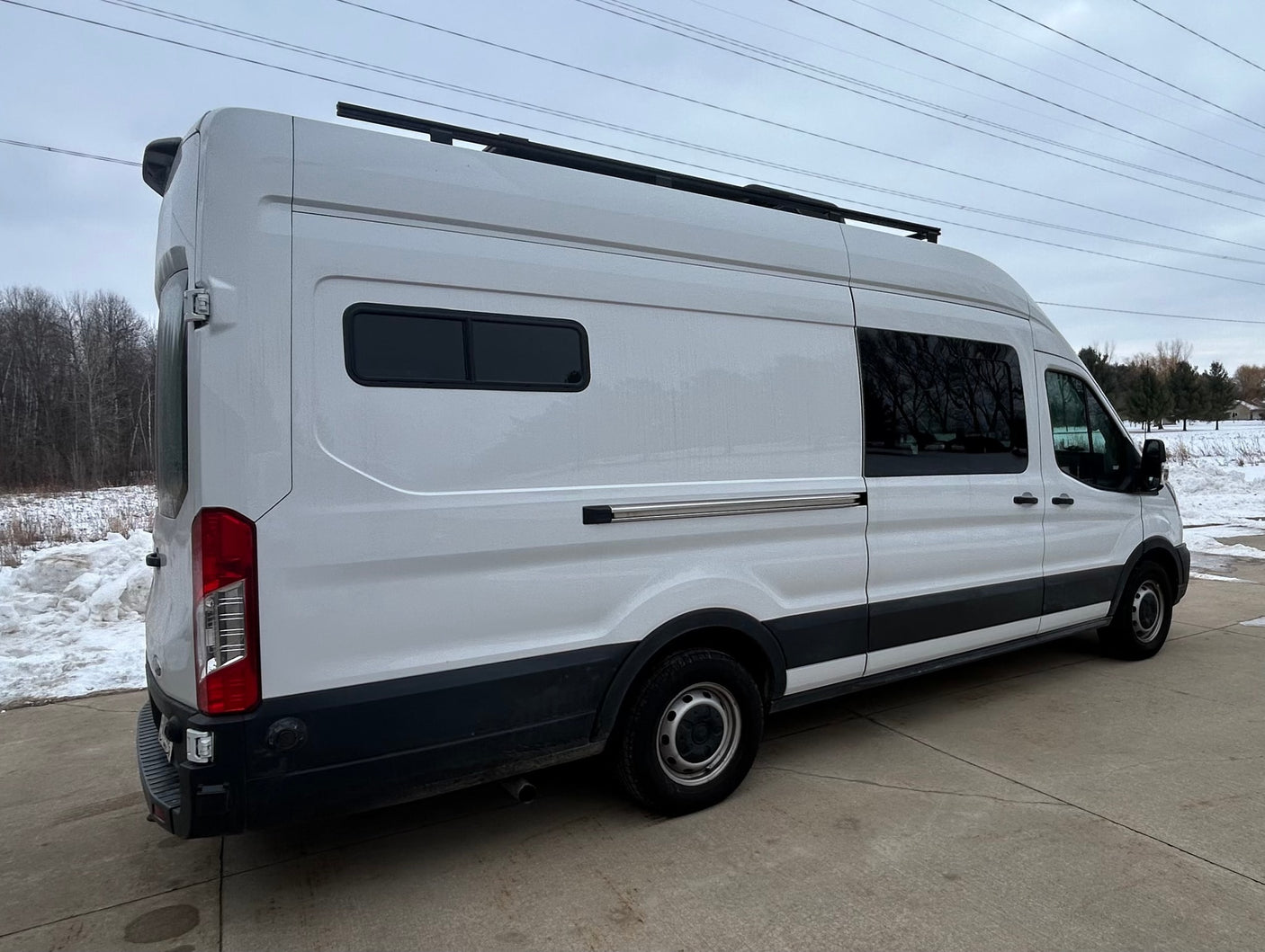 White Ford Transit camper van with custom tinted windows, roof rack & rear camera, ideal for rv rental adventures.