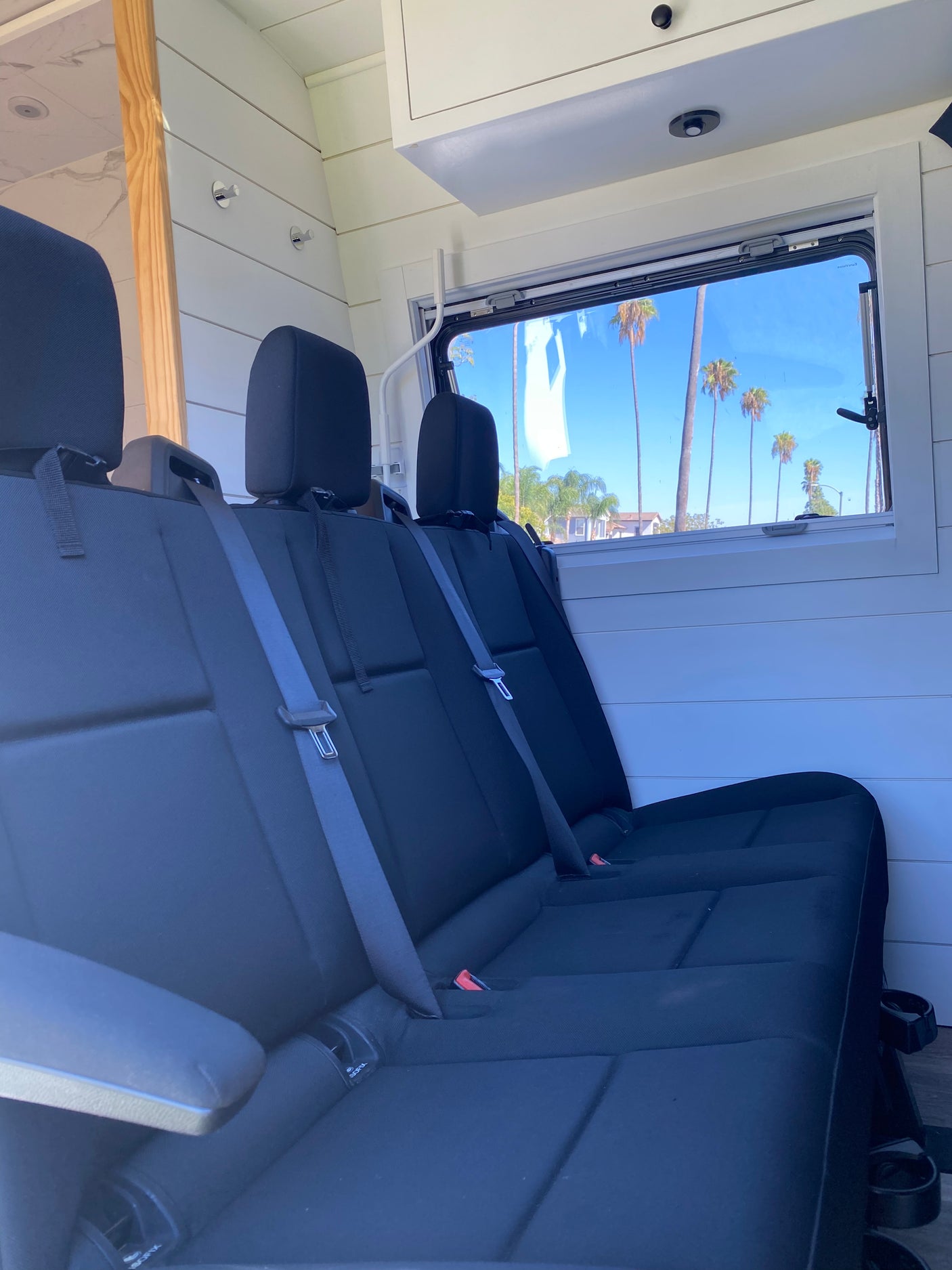 Spacious RV rental interior featuring black passenger seats, white paneling, and a sunny window view with palm trees.