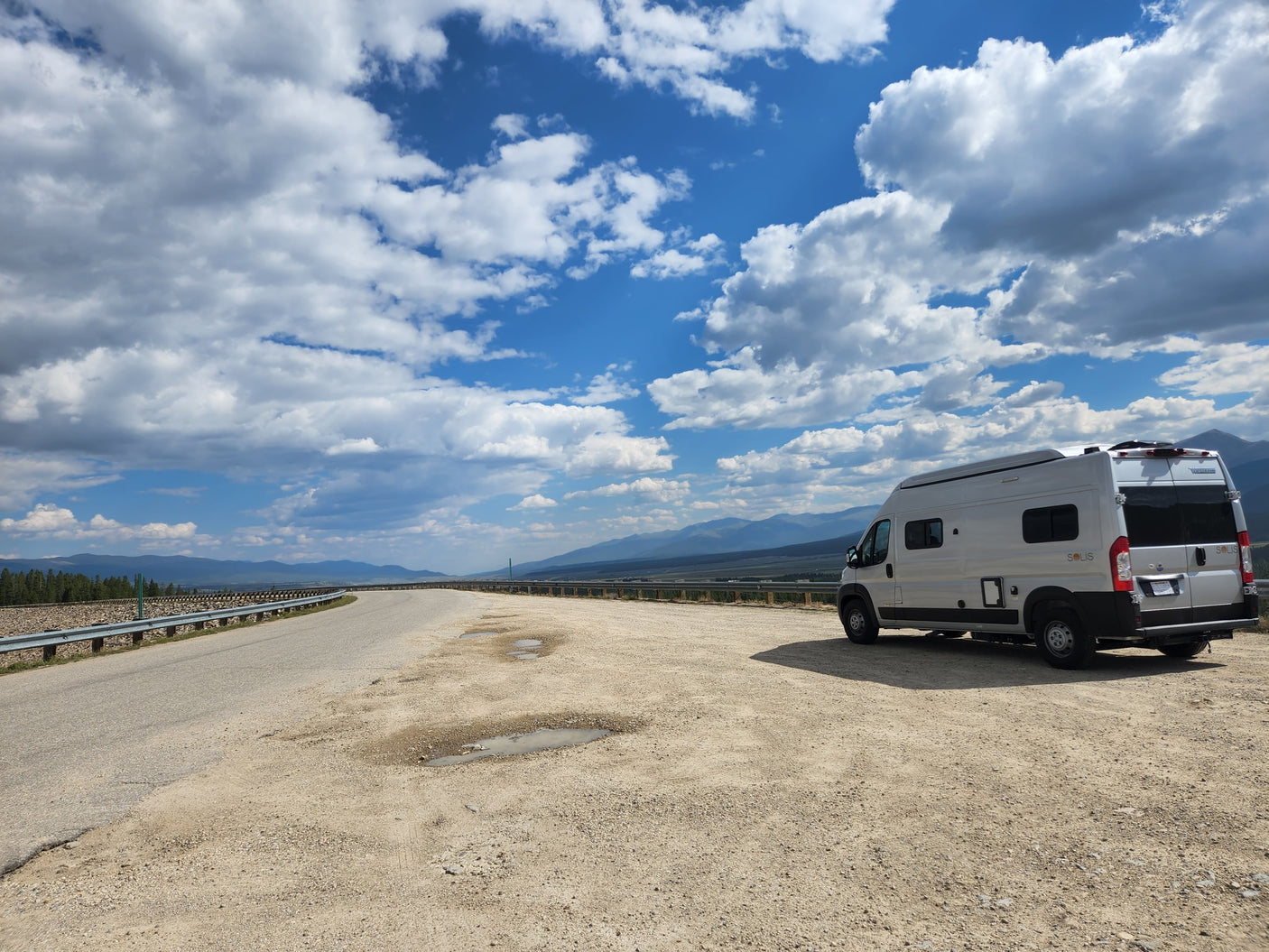 Silver RV rental parked at a scenic mountain overlook. Winding road
