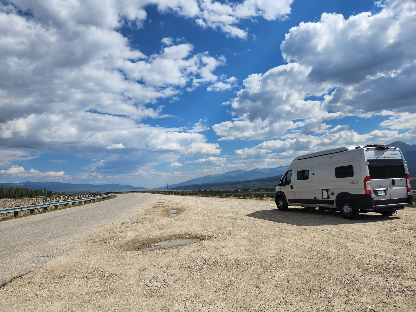 Silver RV rental parked at a scenic mountain overlook. Winding road